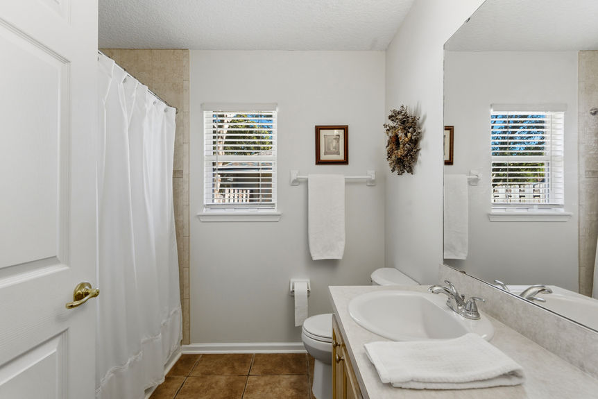 Homes for Sale in St. Johns, Florida: A clean second bathroom featuring a light wood vanity, neutral tile flooring, a large mirror, and a window providing natural light.