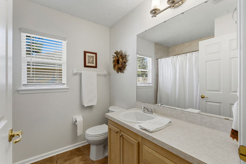 Homes for Sale in St. Johns, Florida: A clean second bathroom featuring a light wood vanity, neutral tile flooring, a large mirror, and a window providing natural light.