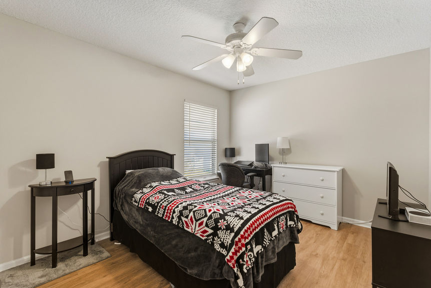 Homes for Sale in St. Johns, Florida: A clean secondary bedroom featuring wood-style flooring, a dark wood bed frame with a festive blanket, a white dresser, and a dedicated desk area.
