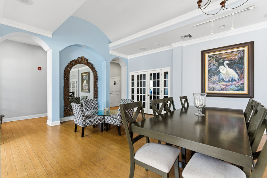 Elegant community dining area in the Harbour Vista Cir clubhouse featuring a large wood table, blue arched accents with an oversized mirror, and bamboo-style wood flooring in St. Augustine, FL.
