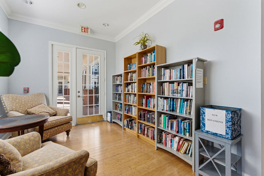 Resident library and reading room at the Harbour Vista Cir clubhouse with tall oak bookshelves and tan armchairs.