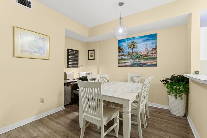 A dining area with a white wooden table set under a pendant light, adjacent to a breakfast bar and kitchen.