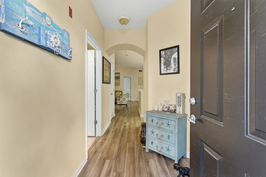 An interior view of the foyer with wood-style flooring, a light blue accent chest, and coastal-themed wall decor.