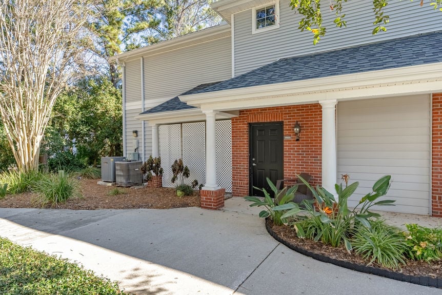 A paved walkway leading to the entrance of a grey-sided condo building with red brick accents in St. Augustine.