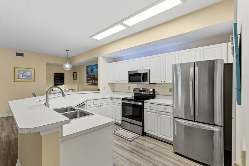 Modern white kitchen with stainless steel appliances and breakfast bar in a St. Augustine condo.