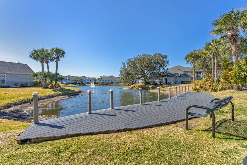 A grey wooden boardwalk and viewing bench overlooking the central community lake and fountain in St. Augustine, FL.