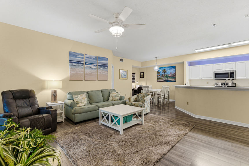 A living room with a green sofa, patterned armchair, and glass doors leading to a screened-in balcony.