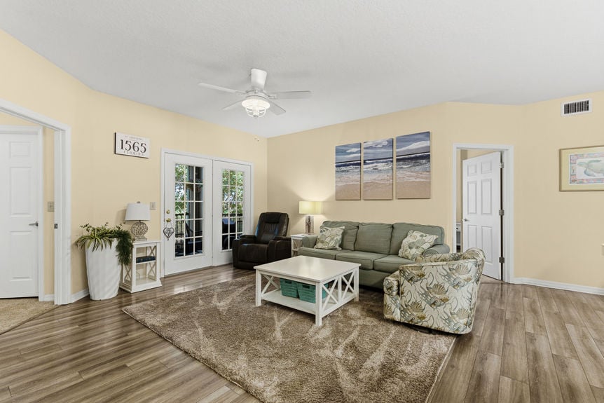A living room with a green sofa, patterned armchair, and glass doors leading to a screened-in balcony.