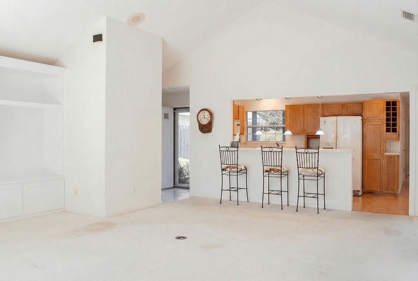 Interior view of 364 Village Dr in St. Augustine, FL, showing a spacious living room with vaulted ceilings and a built-in entertainment center that flows into an open kitchen with a raised breakfast bar and seating.