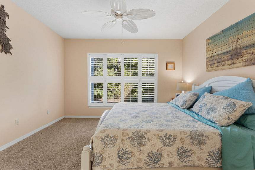 Spacious primary bedroom at 35103 Harbour Vista Cir, St. Augustine, featuring a white wooden bed frame, neutral carpet, and views through plantation shutters.