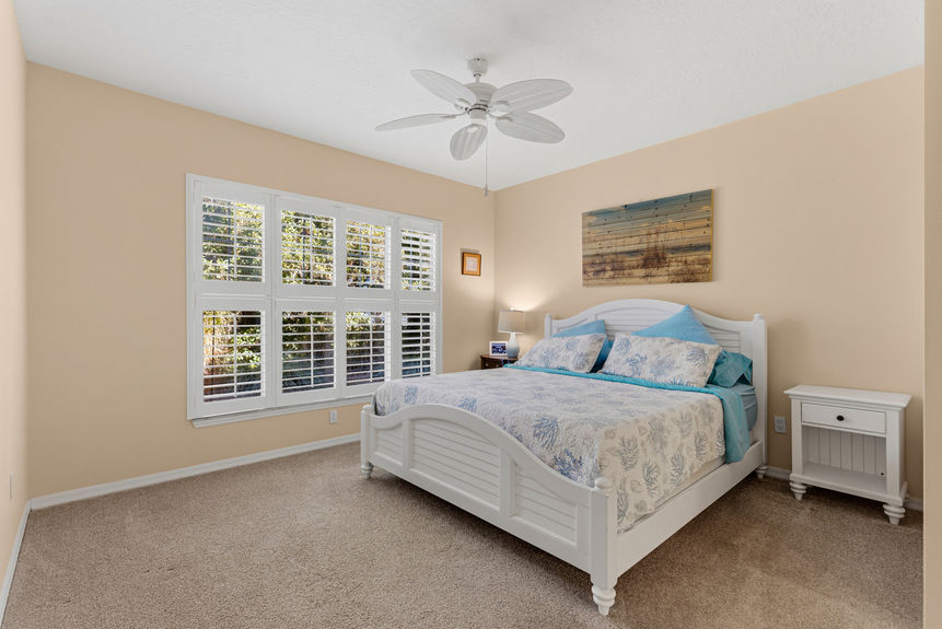 Spacious primary bedroom at 35103 Harbour Vista Cir, St. Augustine, featuring a white wooden bed frame, neutral carpet, and views through plantation shutters.