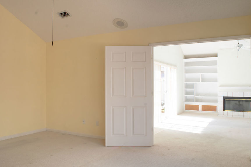 Interior of a bedroom at 364 Village Dr in St. Augustine, Florida, featuring light yellow walls and a view into the bright, open living area with a fireplace and built-in shelving.