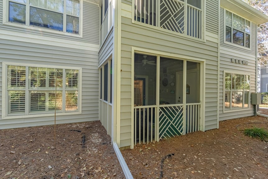 Ground-floor screened-in porch at 35103 Harbour Vista Cir in St. Augustine, FL, featuring a wood-beam ceiling, ceiling fan, coastal rug, and black wicker patio furniture overlooking a wooded area.