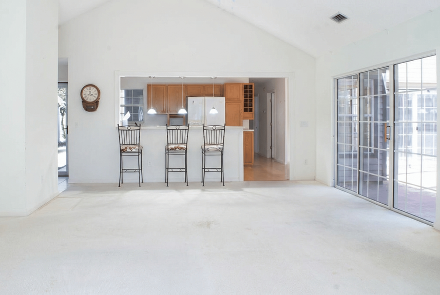 A view of the open-concept living room at 364 Village Dr, St. Augustine, featuring vaulted ceilings, a kitchen breakfast bar with seating, and sliding glass doors leading to a private patio in the Villages of Vilano community.