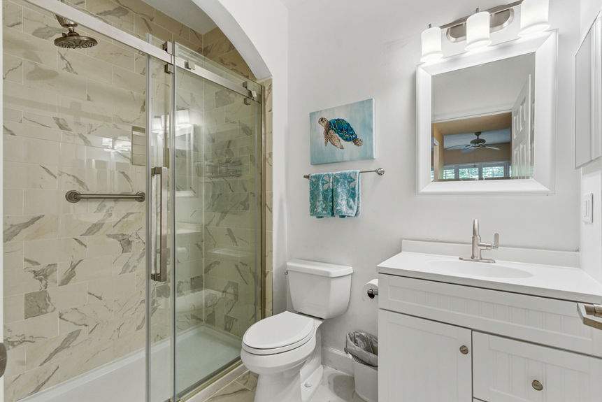 Modernized bathroom at 35103 Harbour Vista Cir featuring a walk-in glass-enclosed shower with marble-style tile, a white vanity, and nautical sea turtle artwork in St. Augustine, FL.