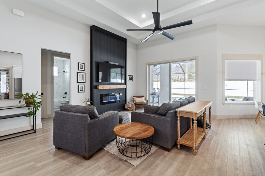 Living room featuring a stunning black shiplap focal wall with a built-in electric fireplace and large TV, overlooking the pool.