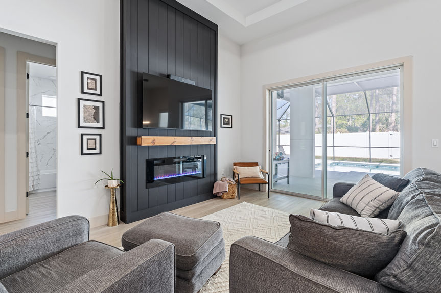Modern living room featuring a black shiplap electric fireplace wall with wood mantel and sliding glass doors to a pool.