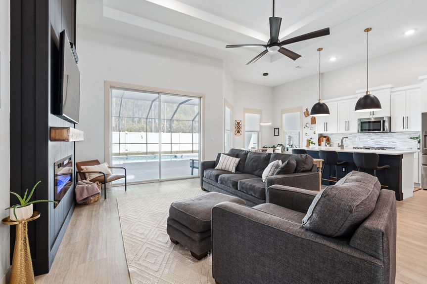 Wide-angle view of an open concept great room with tray ceilings, modern ceiling fan, and a chef's kitchen in the background.