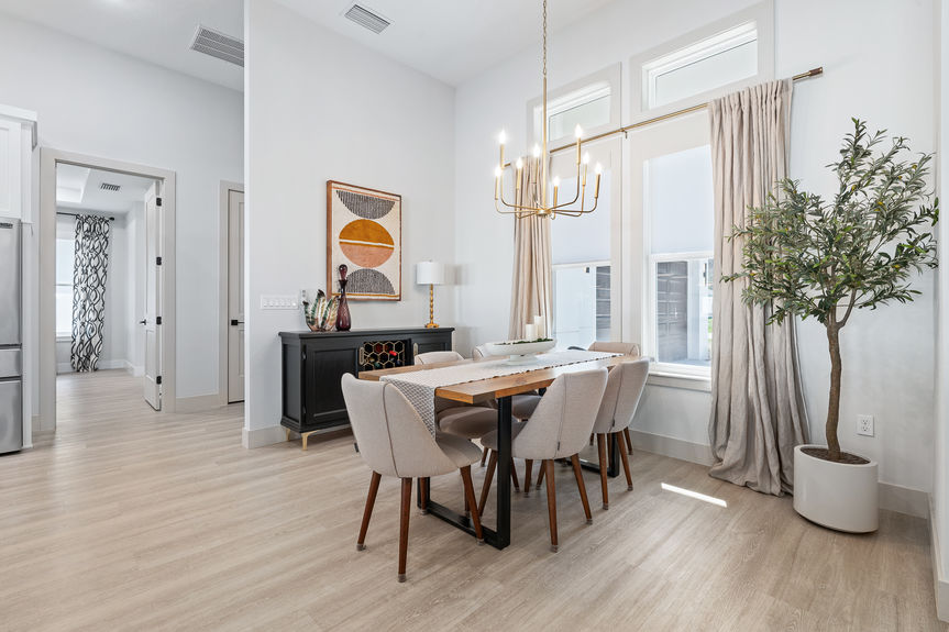 Formal dining space with a natural wood table, gold chandelier, and a large black sideboard against a minimalist white wall.
