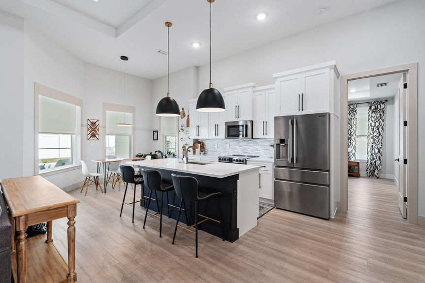 Modern kitchen featuring a large black center island, white cabinetry, stainless steel appliances, and stylish black pendant lights.
