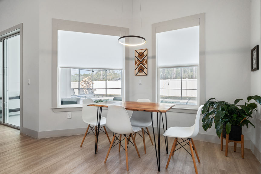 A sun-drenched dining nook with a live-edge wood table, white mid-century chairs, and a halo light fixture in a modern Florida home.