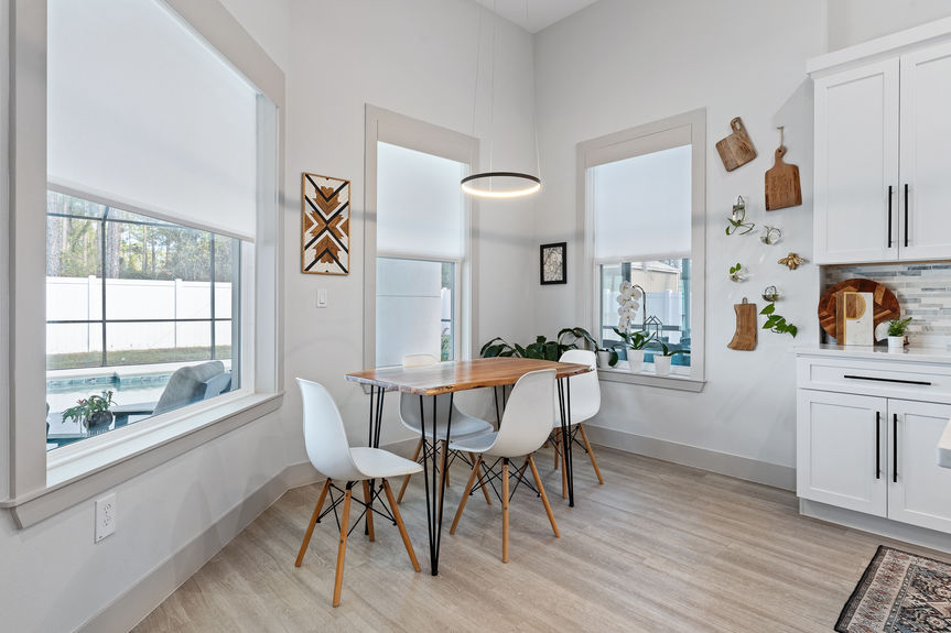 Close-up of a modern dining nook featuring white Eames-style chairs and large windows looking out toward a private screened-in pool.