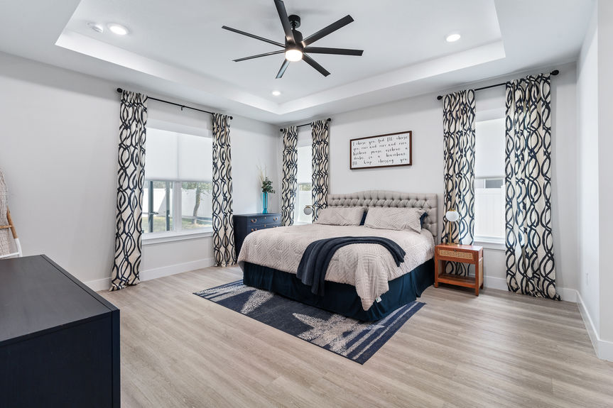Large primary suite with a tray ceiling, king-size bed, blue coastal decor, and modern ceiling fan in a Palm Coast, FL home.