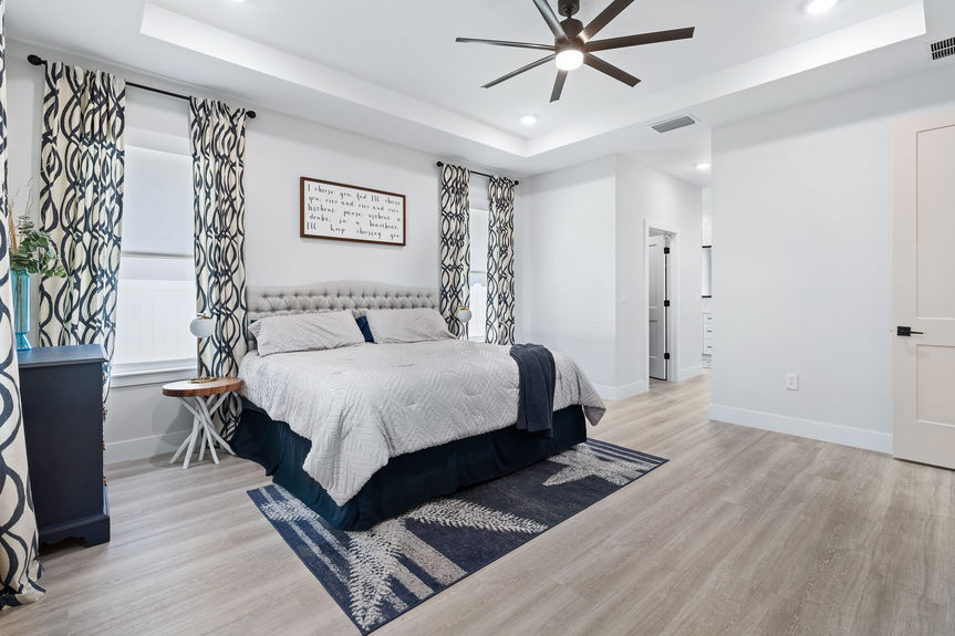 Large primary suite with a tray ceiling, king-size bed, blue coastal decor, and modern ceiling fan in a Palm Coast, FL home.