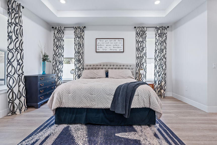 Large primary suite with a tray ceiling, king-size bed, blue coastal decor, and modern ceiling fan in a Palm Coast, FL home.