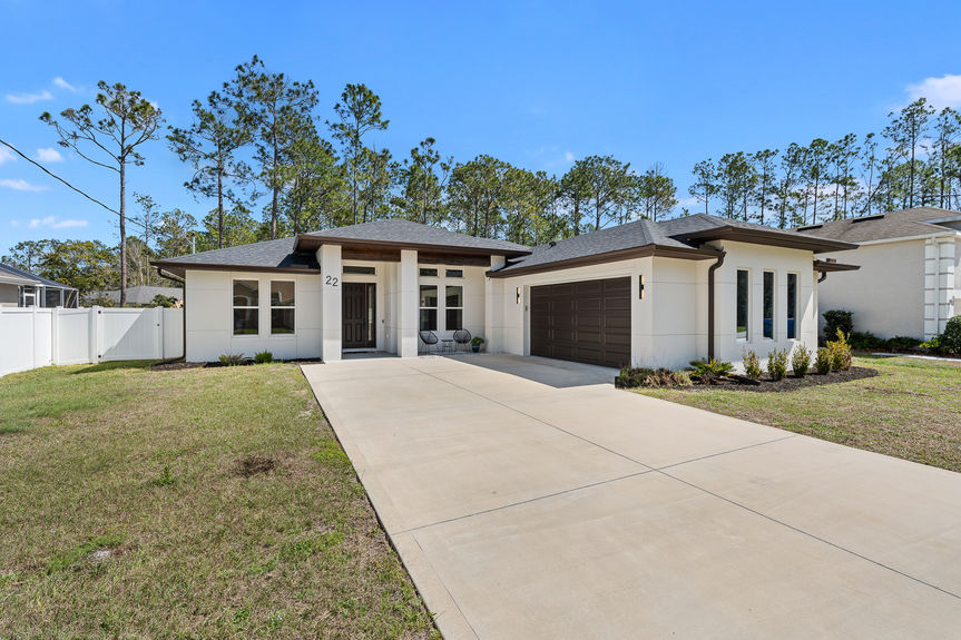 Angled front exterior shot of a modern home showing the dark garage door, white concrete block walls, and clean architectural lines.