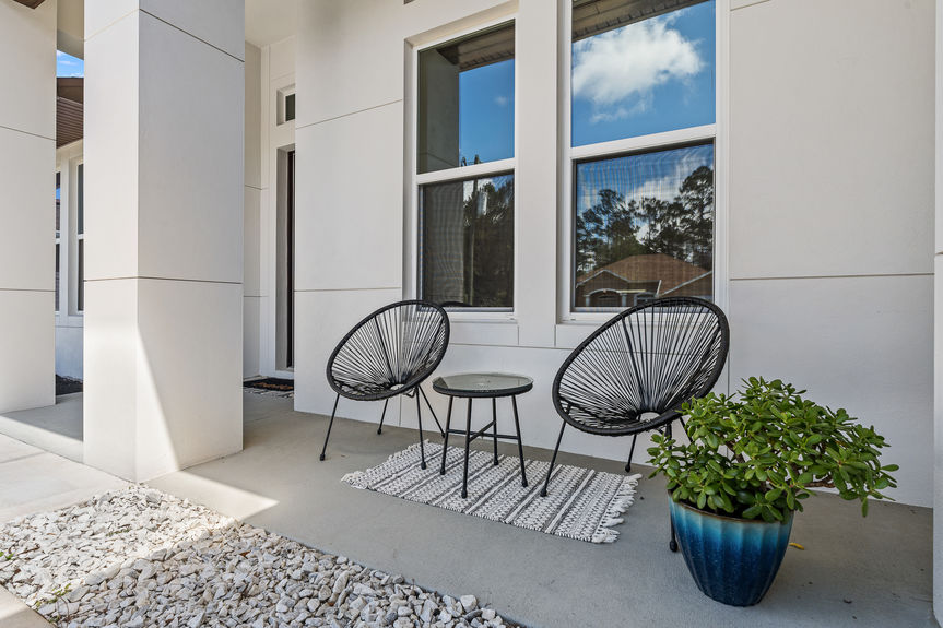 Close-up of a cozy porch seating arrangement with black chairs and a 'hello' doormat, highlighting the clean white exterior finishes.