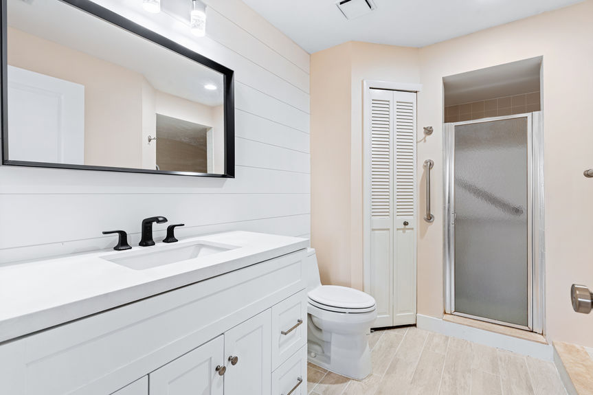 Renovated bathroom featuring a dark wood vanity, white marble countertop, and a modern LED-backlit mirror.