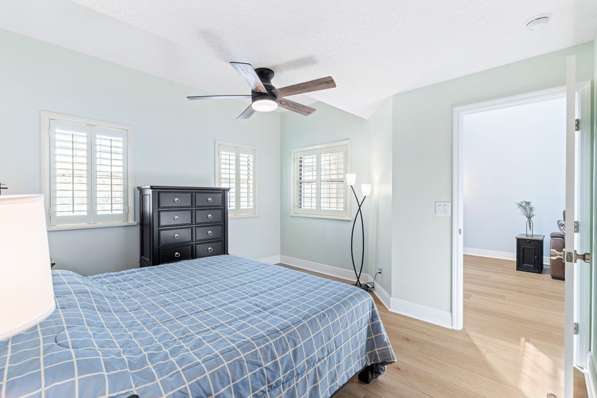 Master bedroom showing a dark wood dresser and bed frame with white plantation shutters and new flooring at 37 Captains Walk.