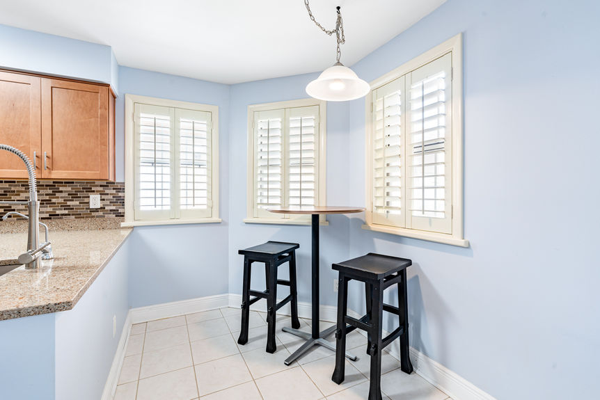 A cozy breakfast nook off the kitchen with three windows featuring plantation shutters and a bistro-style high table.