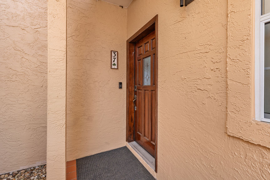 Front exterior of a tan stucco waterfront condo at 37 Captains Walk with palm trees and a paved walkway in Palm Coast, FL.