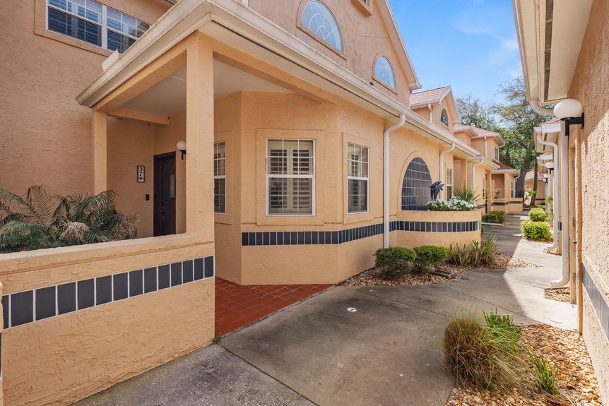 Front exterior of a tan stucco waterfront condo at 37 Captains Walk with palm trees and a paved walkway in Palm Coast, FL.