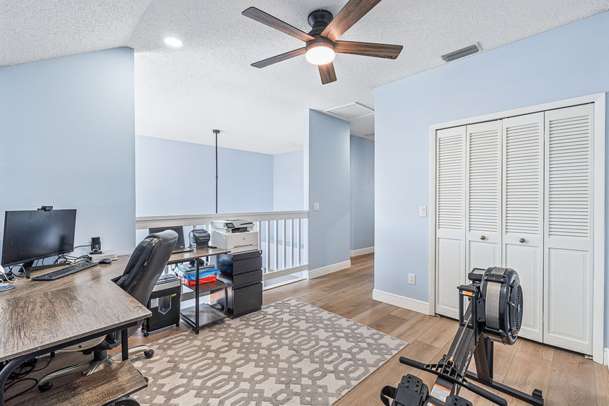 Ofice A spacious upper-level loft at 37 Captains Walk featuring a home office desk, rowing machine, and new wood-look flooring overlooking the living area.