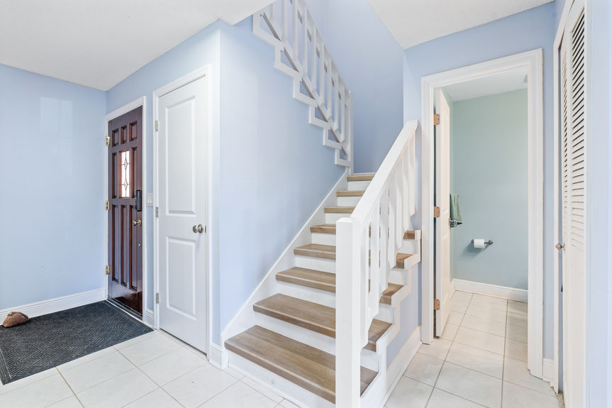 The entryway of 37 Captains Walk showing the front door and a staircase featuring updated wood-style steps and light blue walls.