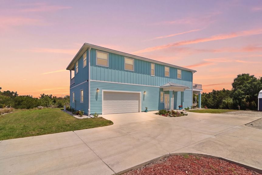 unset exterior view of 5900 Costanero Road, a light blue two-story coastal home in St. Augustine, Florida, featuring a large concrete driveway and 2-car garage.