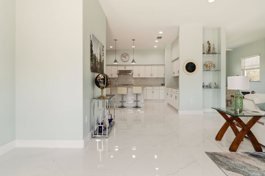 Interior view of the open-concept living room and kitchen at 5900 Costanero Road, featuring white marble-look tile floors and light mint green walls.