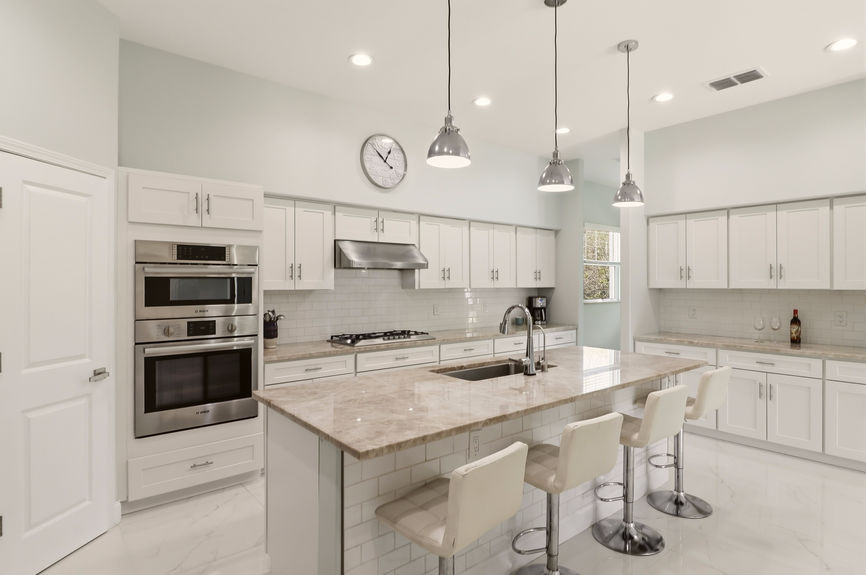 Modern kitchen at 5900 Costanero Road featuring white cabinets, stainless steel appliances, stone countertops, and a large center island with seating.