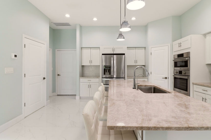 Modern kitchen at 5900 Costanero Road featuring white cabinets, stainless steel appliances, stone countertops, and a large center island with seating.