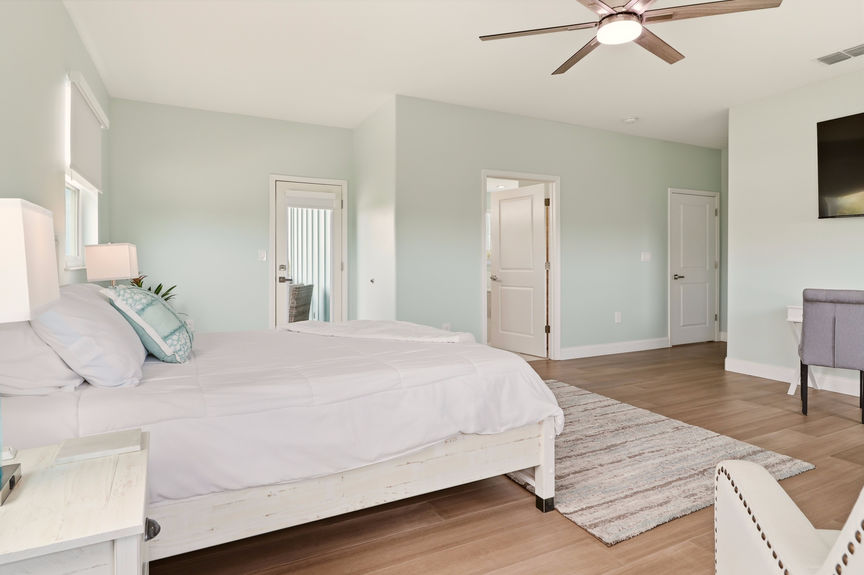 Large primary bedroom at 5900 Costanero Road with light blue walls, wood-look flooring, a sitting area with two cream armchairs, and large windows.