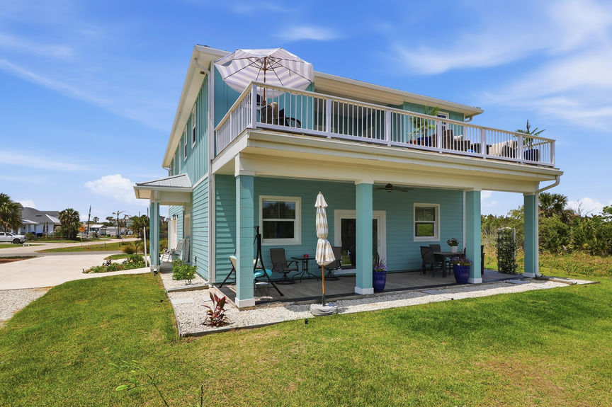 Side profile of 5900 Costanero Road showing the expansive second-story balcony and covered ground-floor patio with outdoor furniture in St. Augustine, FL.
