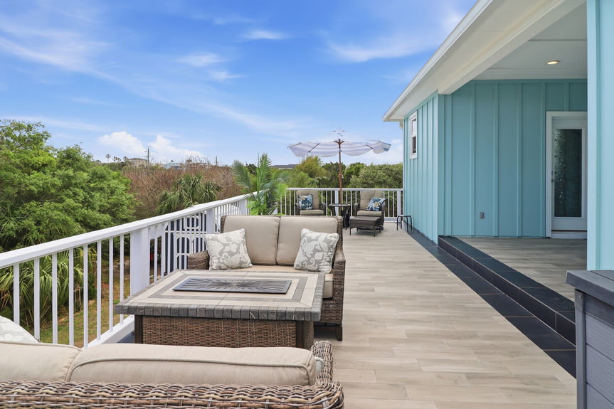 Second-story tiled balcony at 5900 Costanero Road featuring wicker lounge chairs, an umbrella, and views of the lush St. Augustine greenery