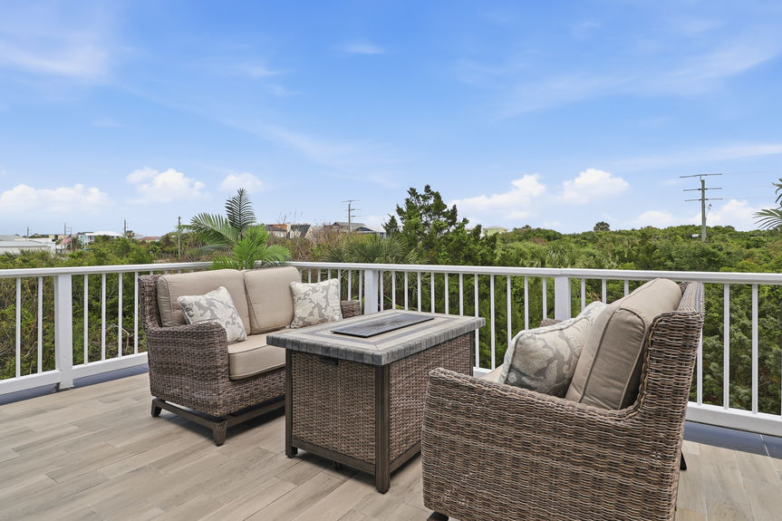Second-story tiled balcony at 5900 Costanero Road featuring wicker lounge chairs, an umbrella, and views of the lush St. Augustine greenery