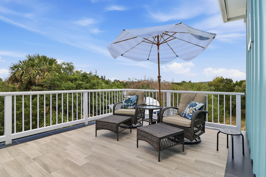 Second-story tiled balcony at 5900 Costanero Road featuring wicker lounge chairs, an umbrella, and views of the lush St. Augustine greenery