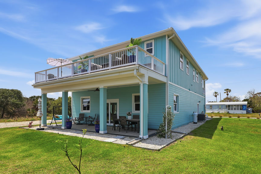 Side profile of 5900 Costanero Road showing the expansive second-story balcony and covered ground-floor patio with outdoor furniture in St. Augustine, FL.