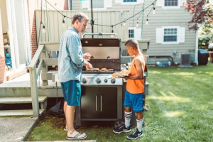 Father and son barbecuing meat on grill in their backyard