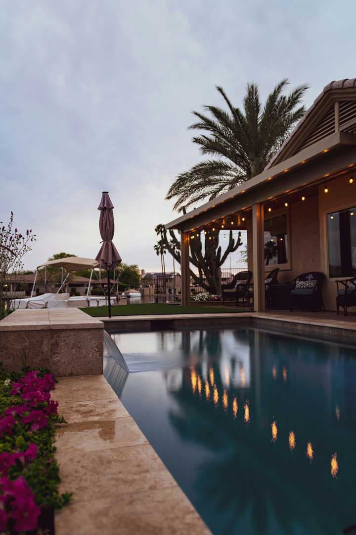 image shows a backyard swimming pool at dusk, with a patio area and a house in the background